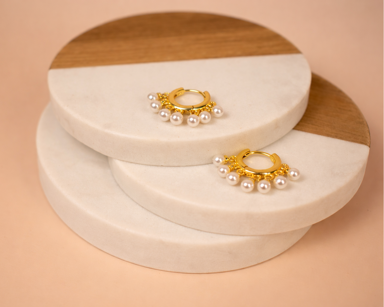Pair of gold and pearl earrings on a stack of round, layered wooden and marble trinket boxes.